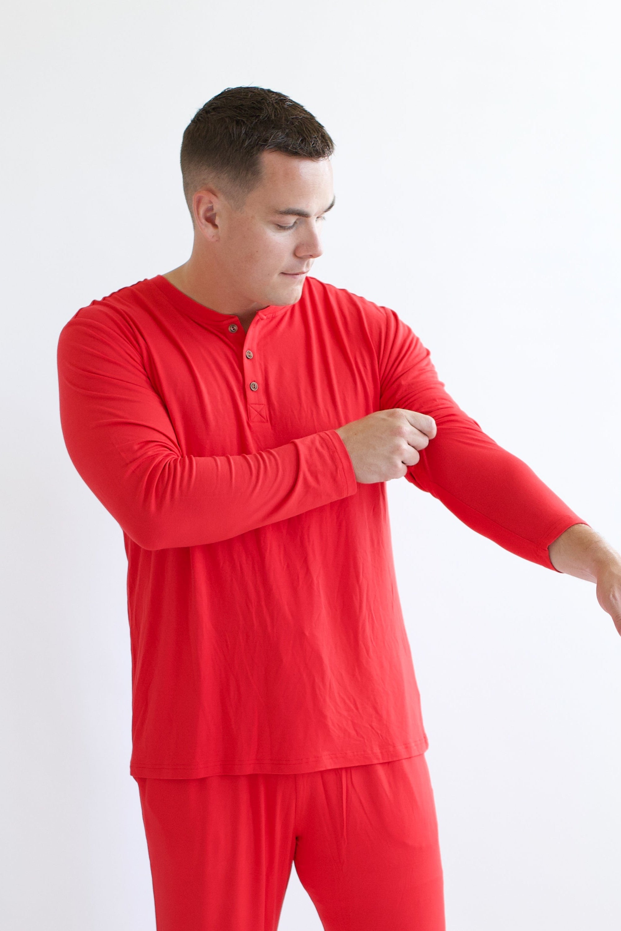 Male model readjusting sleeve while wearing the Men's Long Sleeve Henley Top in Cardinal