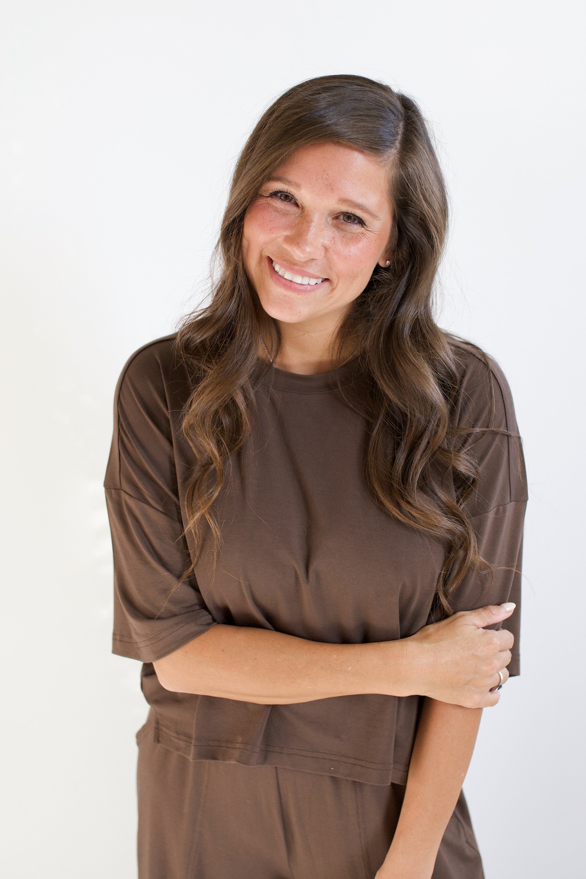 Smiling model with arm across her torso while wearing the Women's Short Sleeve Tee in Espresso