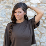 Model with one arm on her head standing in front of a rock wall while wearing the Women's Short Sleeve Tee in Espresso