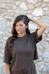 Model with one arm on her head standing in front of a rock wall while wearing the Women's Short Sleeve Tee in Espresso