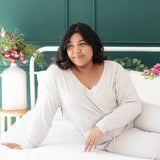 Female sitting on a bed wearing the Women's Ribbed Long Sleeve Crop Top in Oat 