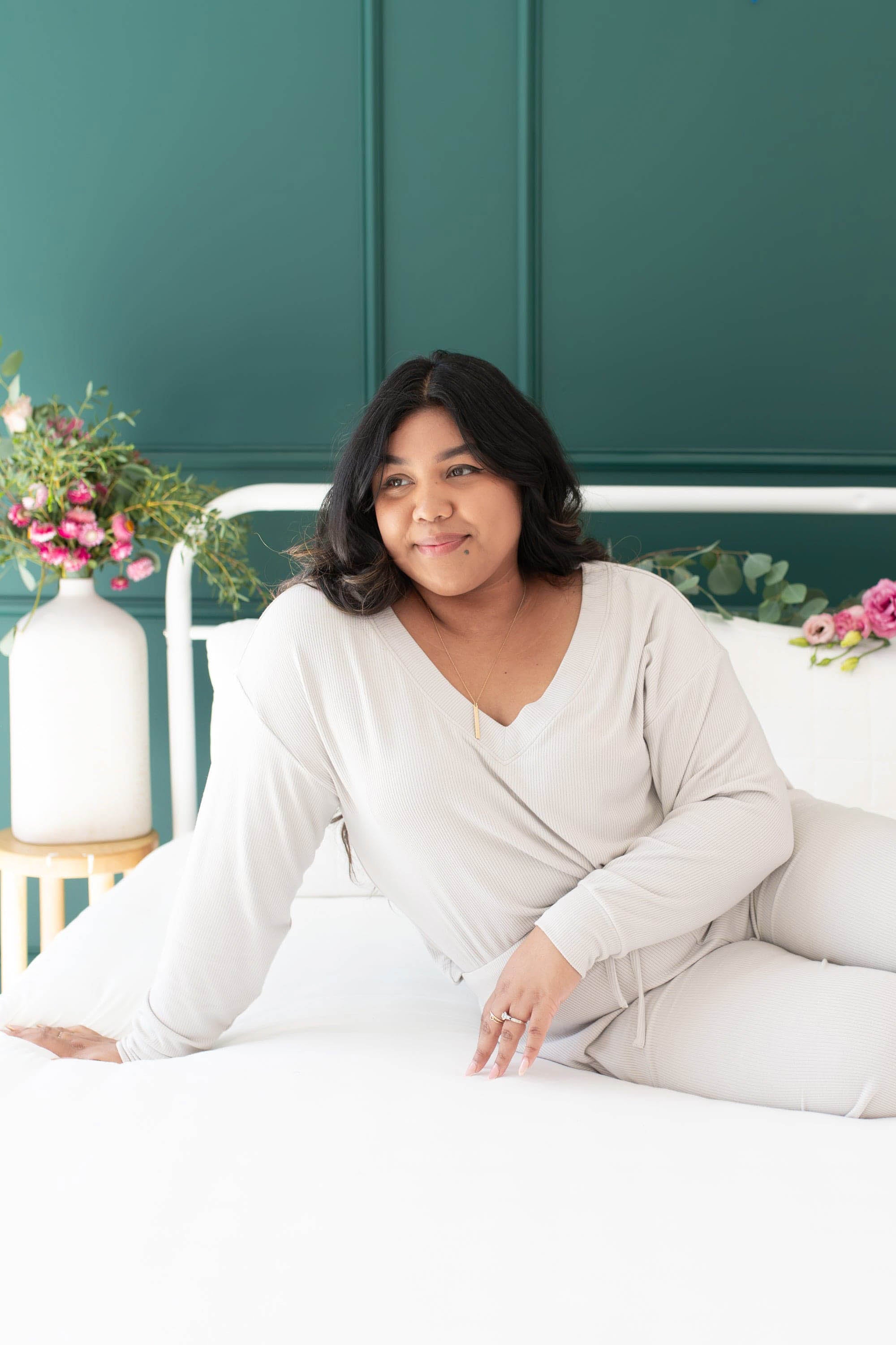 Female sitting on a bed wearing the Women's Ribbed Long Sleeve Crop Top in Oat 