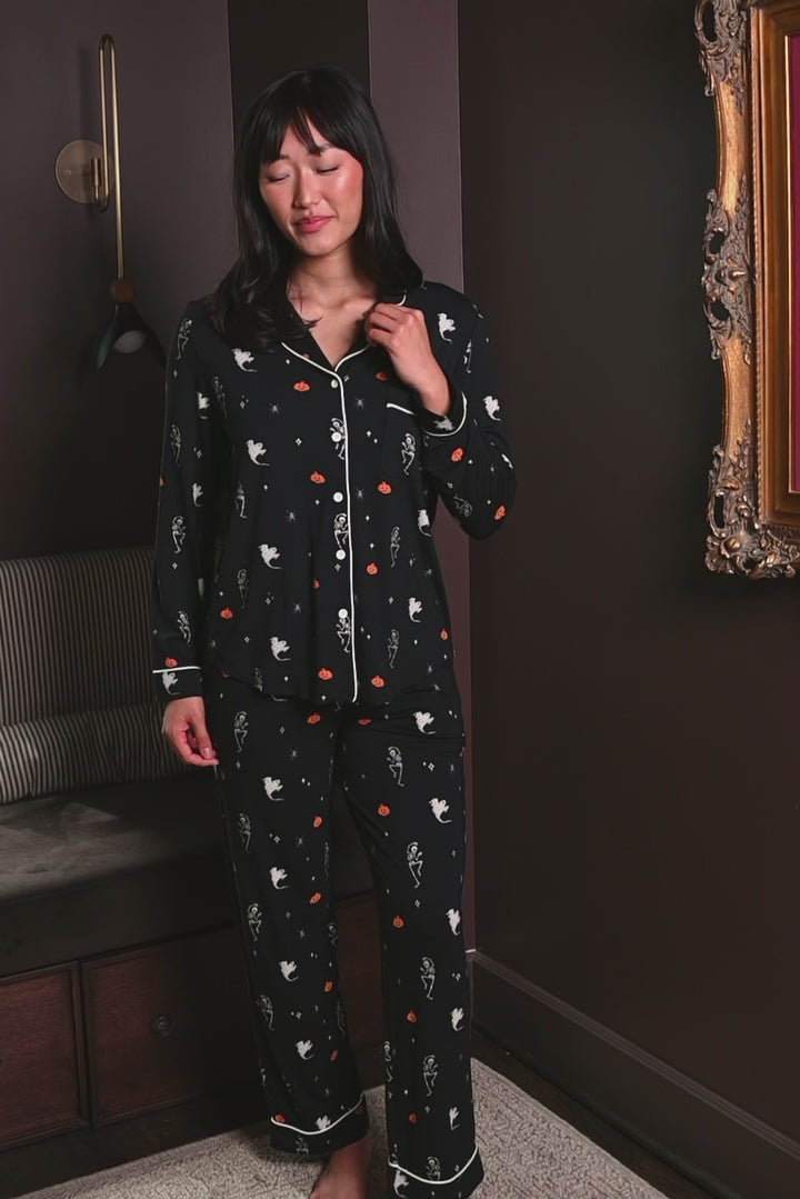 Woman modeling a black pajama set with halloween pattern including pumpkin, ghost and skeleton 