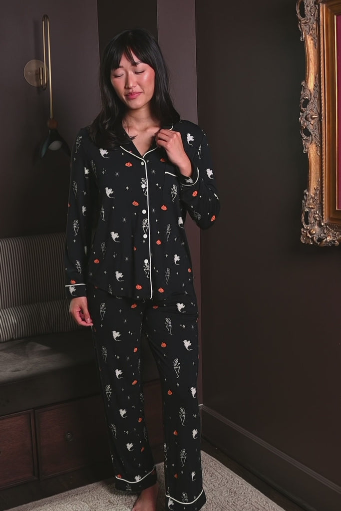 Woman modeling a black pajama set with halloween pattern including pumpkin, ghost and skeleton ::: Model is 5'9" wearing size S /// 