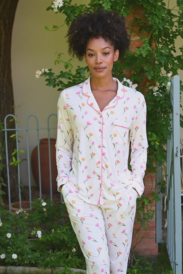 video of Woman in a white tulip pajama set standing on a porch with potted plants. 