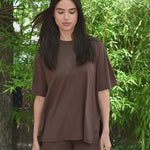 Video of Woman in brown oversized t-shirt and biker shorts standing outdoors with a white fence and trees in the background. ::: Model is 5'10" wearing size S ///