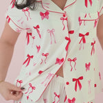 Woman modeling a short sleeve button up pajama set with a red bow print