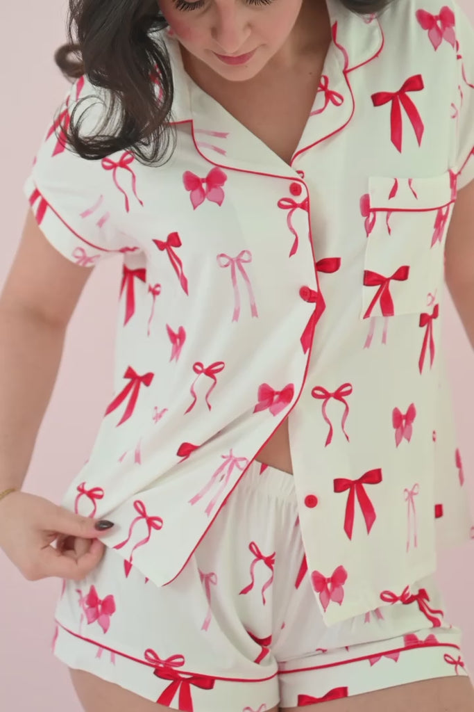 Woman modeling a short sleeve button up pajama set with a red bow print