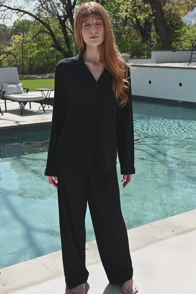 Woman modeling black long sleeve pajamas by a pool  ::: Model is 5'6" wearing size S ///