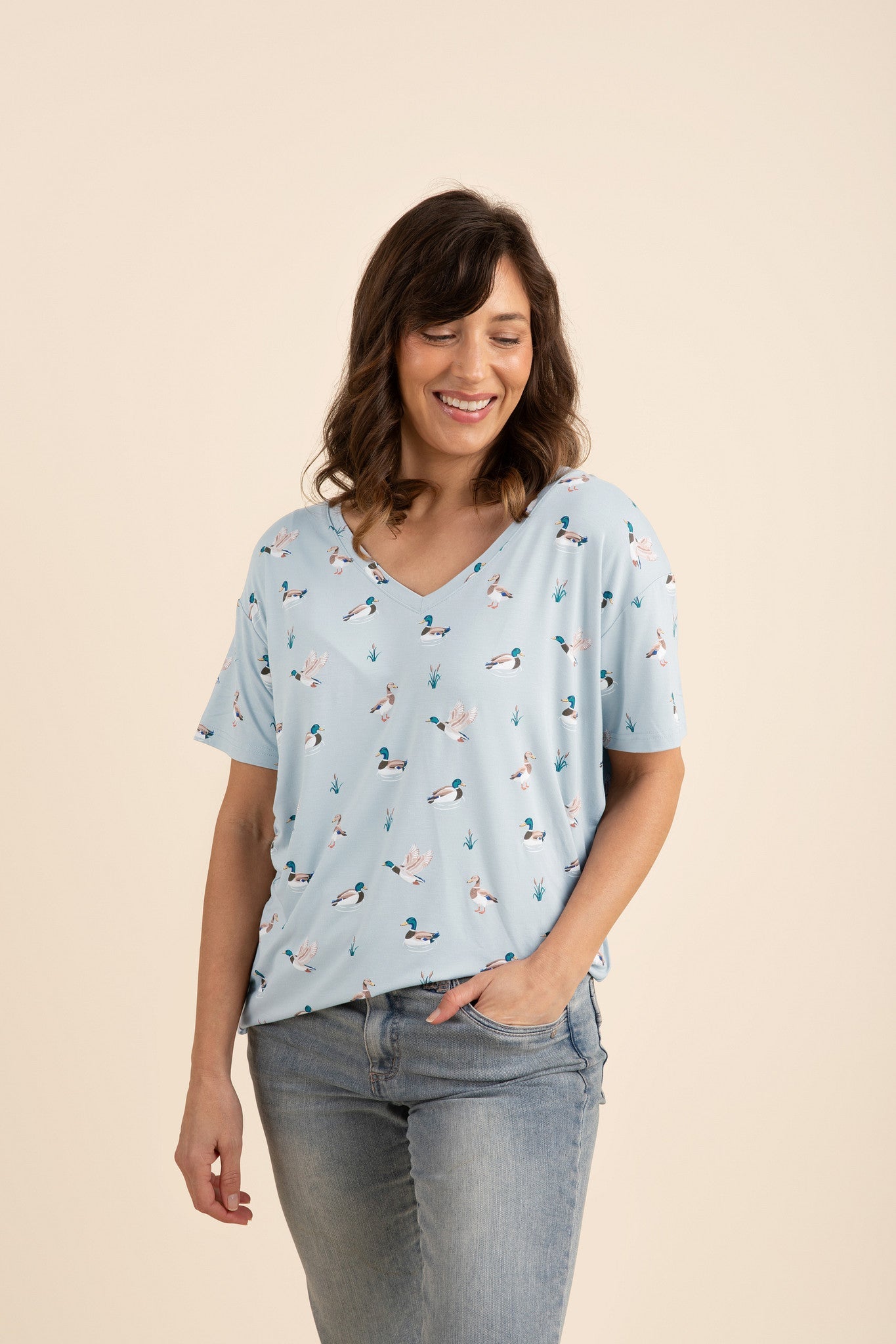 Woman wearing a light blue duck printed v-neck and jeans on a beige background  
