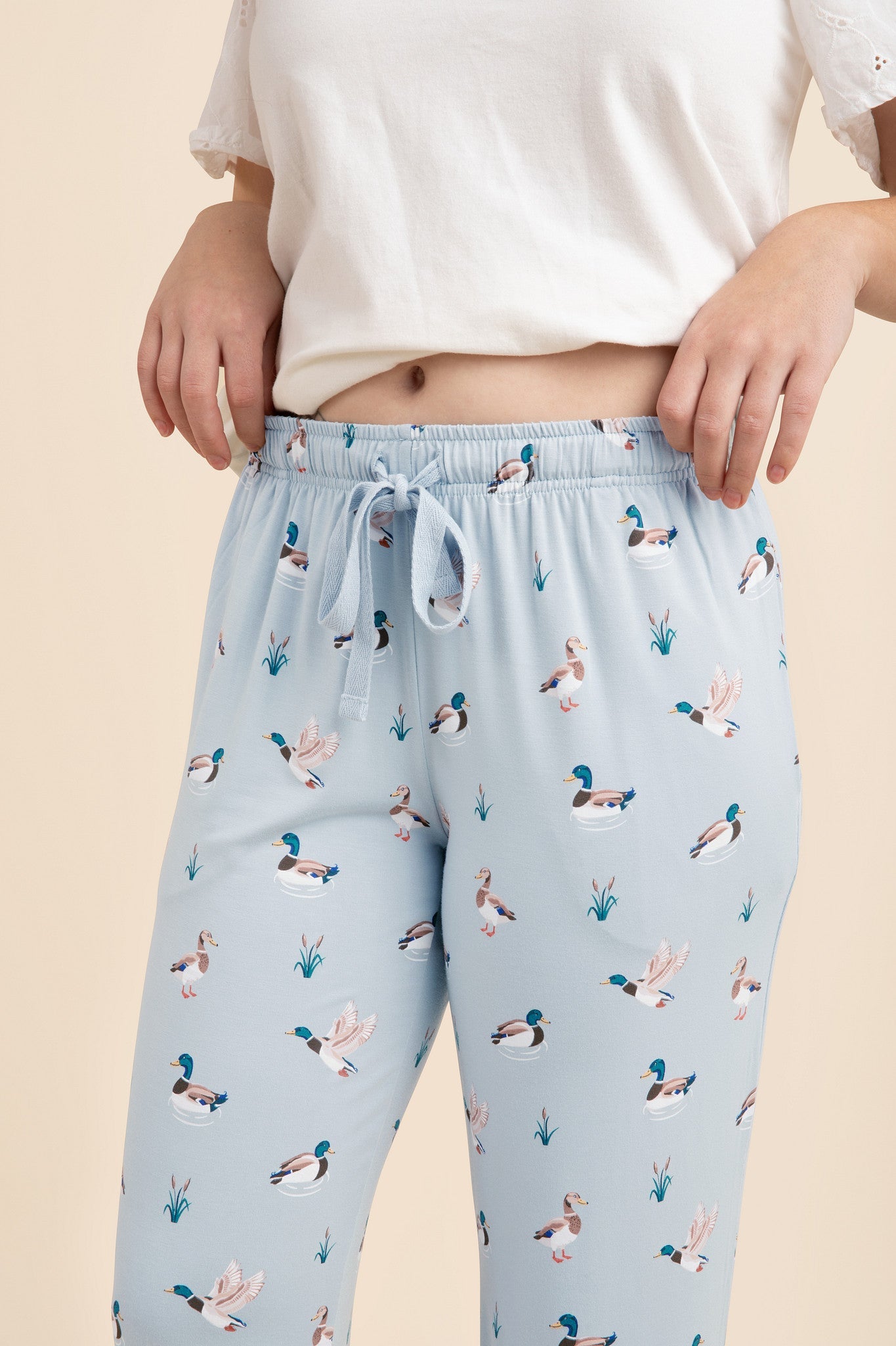 Light blue lounge pants with duck pattern worn by a person on a beige background