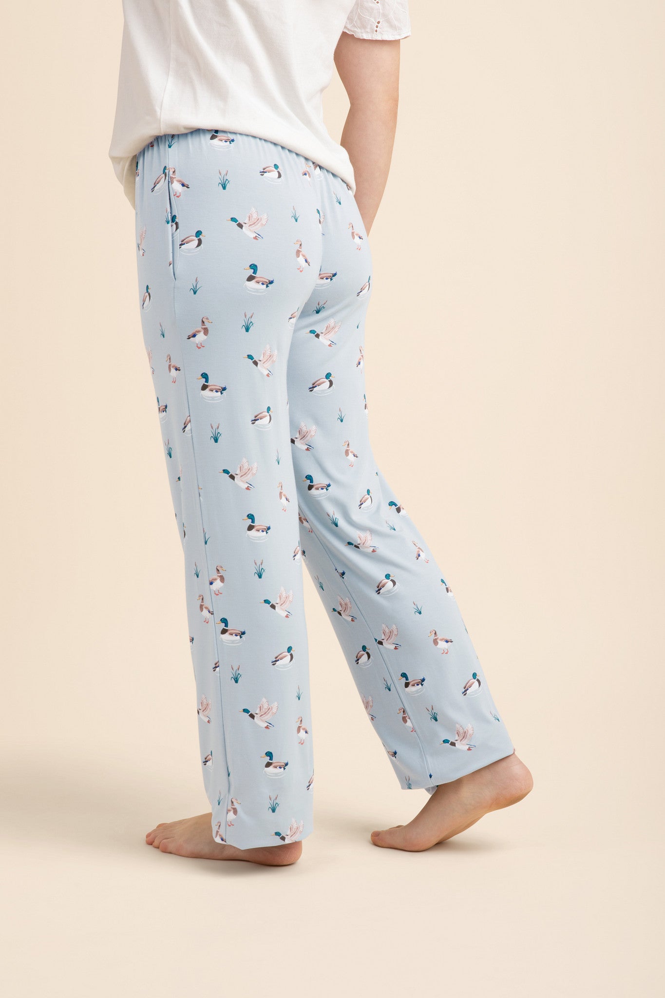 Light blue pajama pants with duck pattern worn by a person on a beige background