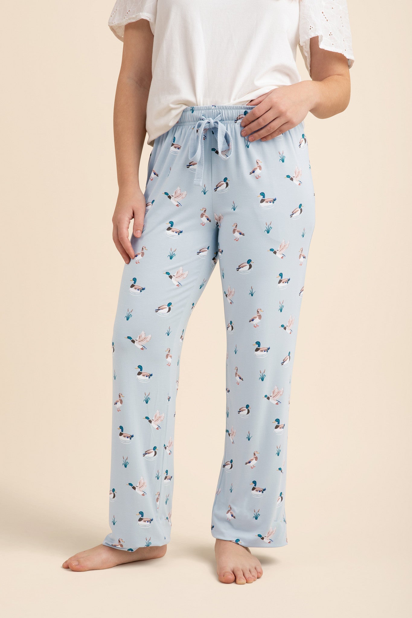Light blue lounge pants with duck pattern worn by a person on a beige background   ::: Model is 5'2" wearing size M ///