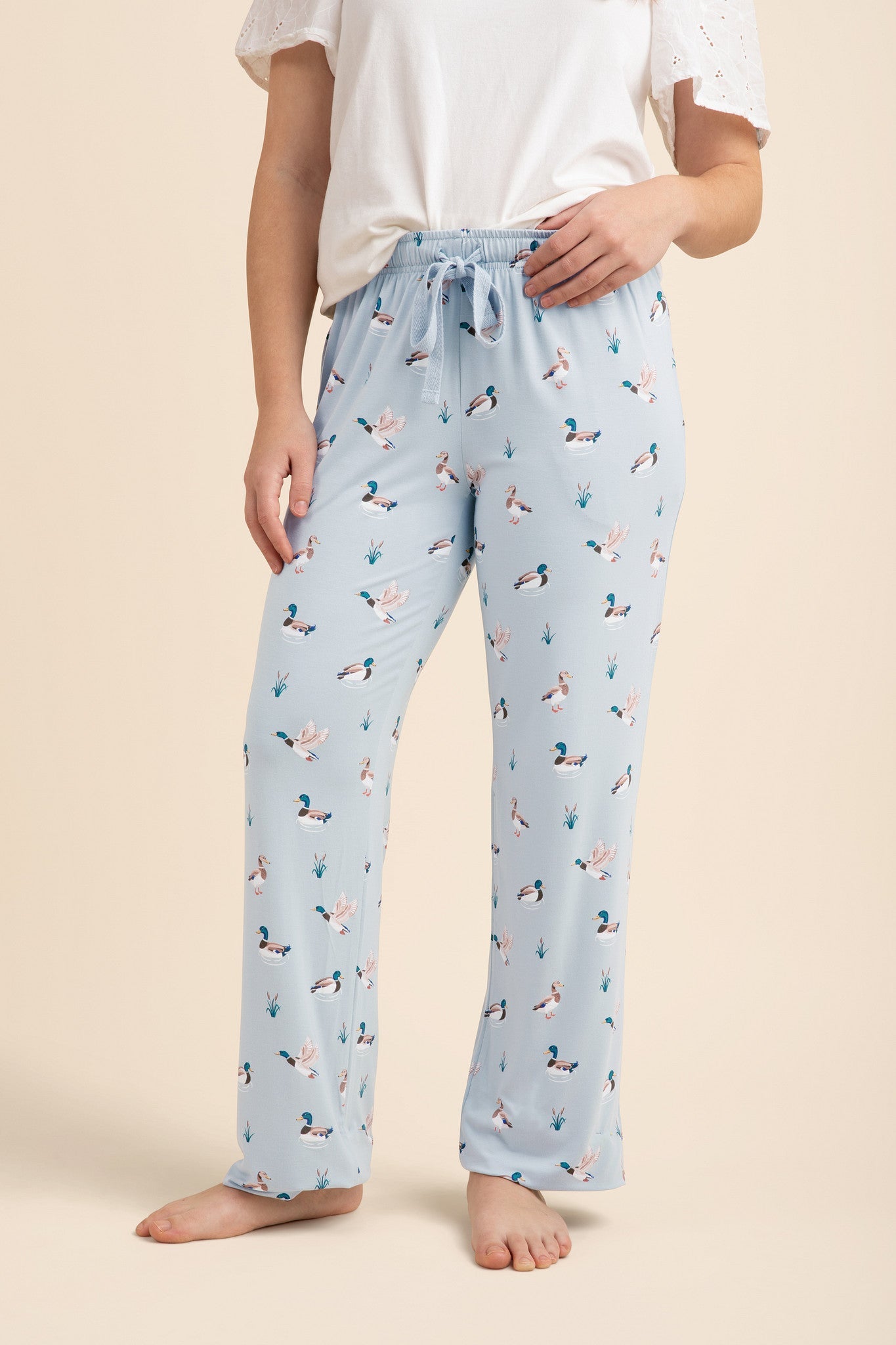 Light blue lounge pants with duck pattern worn by a person on a beige background   
