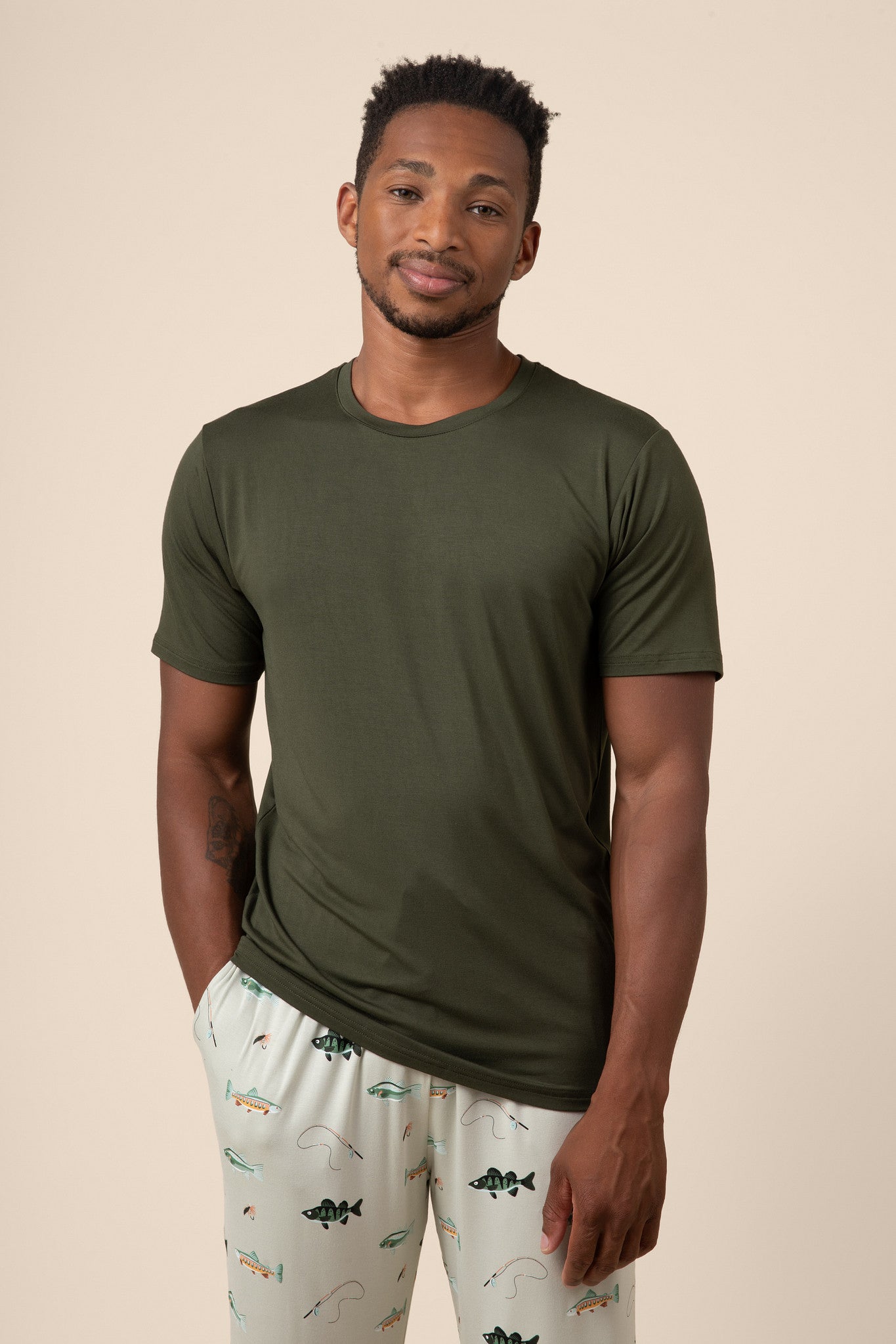 Man wearing dark green Men's Short Sleeve Tee & Pant PJ Set with pocket in Fishing print on a beige background