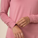 Close-up of a person wearing a pink long-sleeve shirt against a beige background