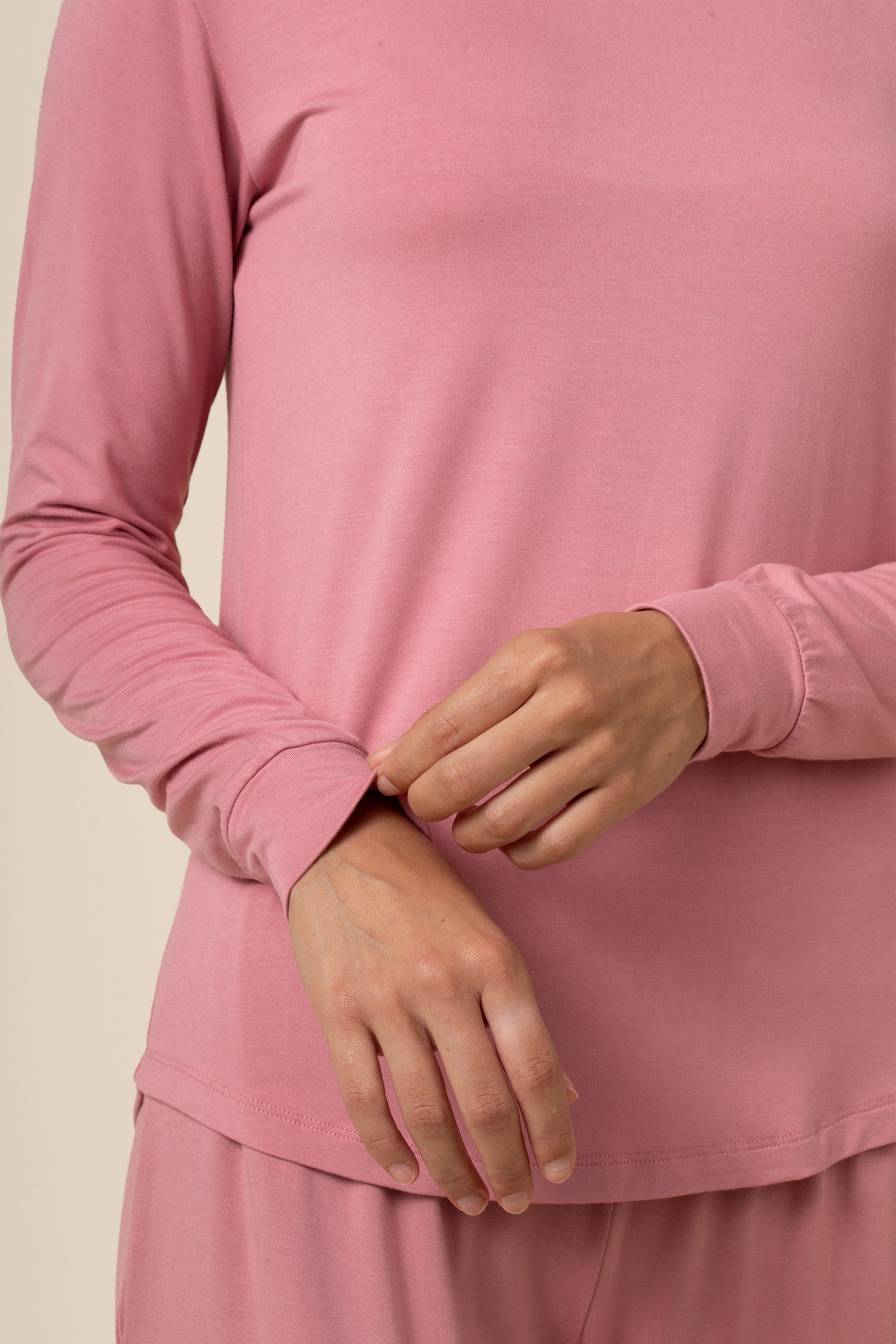 Close-up of a person wearing a pink long-sleeve shirt against a beige background
