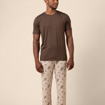 Man wearing a brown t-shirt and western cowboy patterned pants on a beige background