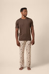 Man wearing a brown t-shirt and western cowboy patterned pants on a beige background