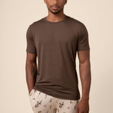 Man wearing a brown t-shirt and western cowboy patterned pants on a beige background