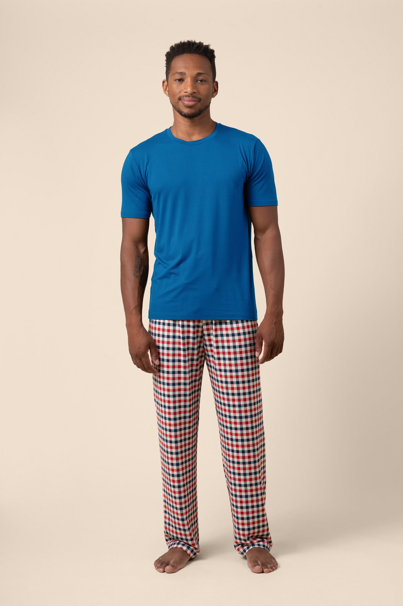 Male model wearing the Men's Lounge Pants in Patriotic Gingham paired with a crew neck in Tahoe while standing in front of a beige background 