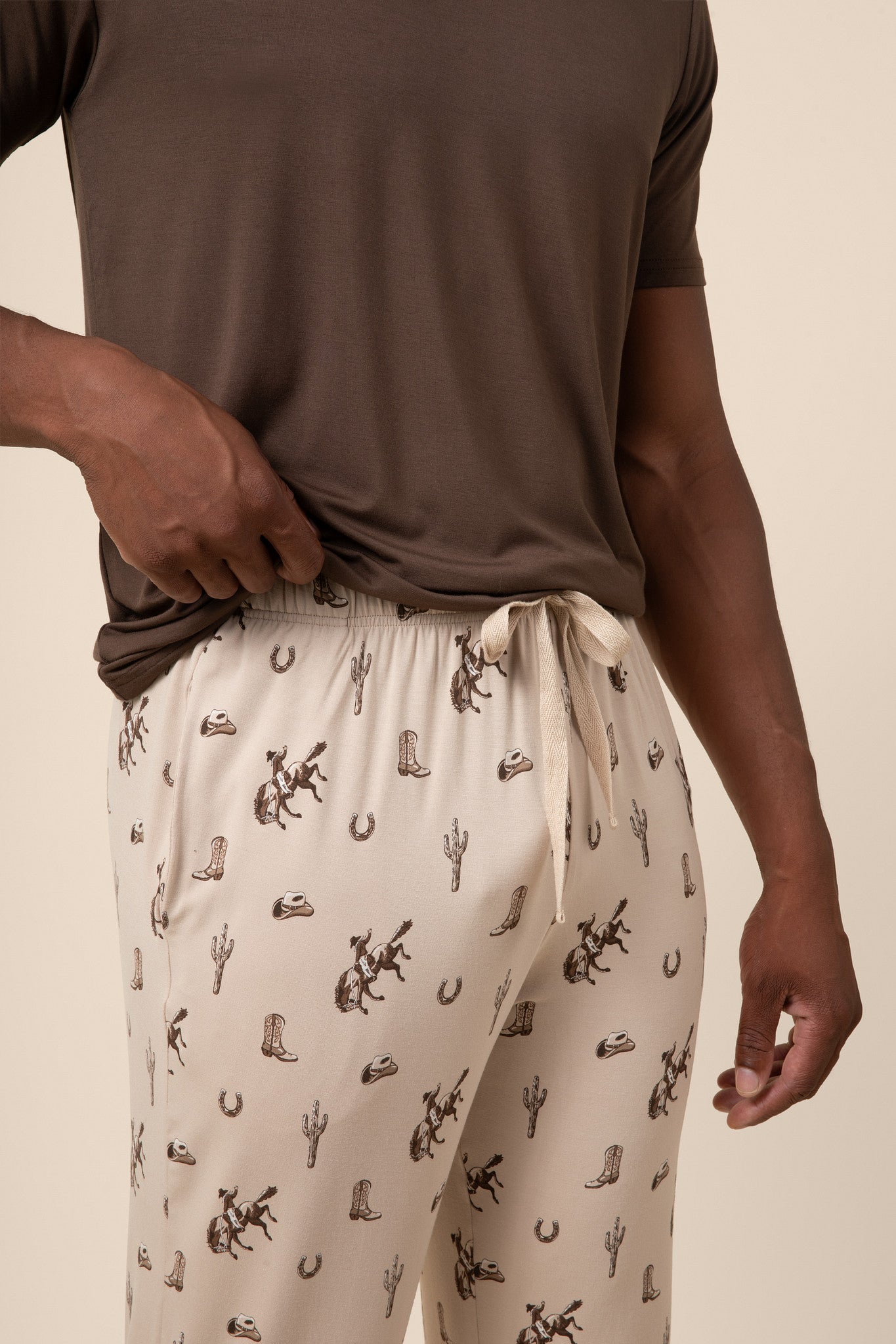 Man showcasing Classic Cowboy patterned pants with drawstring over a brown t-shirt on a beige background