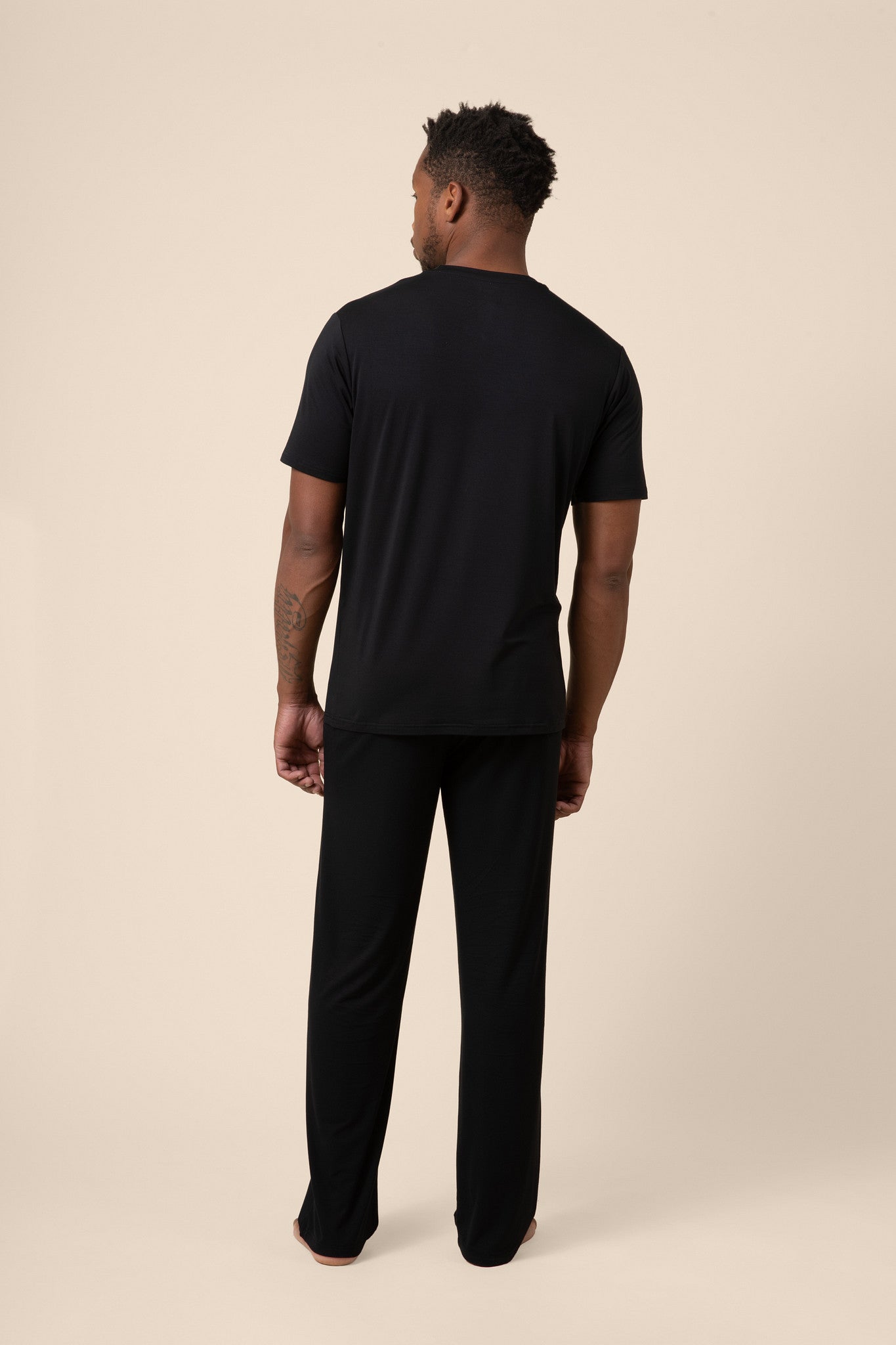 Man showing back side of Black Men's Short Sleeve & Pant PJ Set on beige background