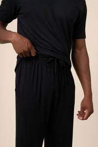 Man showcasing Black PJ pant  with drawstring over Men's short sleeve tee in midnight on beige background